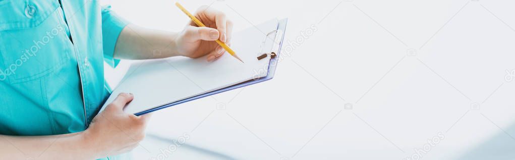 panoramic shot of doctor in blue uniform writing on clipboard