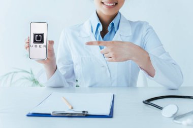 Kiev, Ukrayna - 26 Nisan 2019: Ekranda Uber uygulaması ile akıllı telefon gösteren gülümseyen latin doktor Kırpılmış çekim.