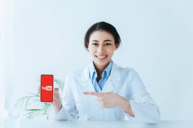 Kiev, Ukrayna - 26 Nisan 2019: Ekranda Youtube uygulaması ile akıllı telefon gösteren neşeli latin doktor.