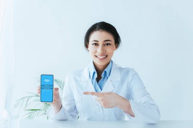 Kiev, Ukrayna - 26 Nisan 2019: Ekranda Skype uygulaması ile akıllı telefon parmak ile işaret Neşeli latin doktor.