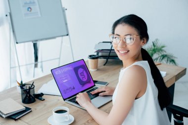 ekranda web-alışveriş web sitesi ile dizüstü bilgisayar kullanırken kameraya bakarak neşeli latin iş kadını