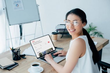 Kiev, Ukrayna - 26 Nisan 2019: Ekranda Airbnb web sitesi ile dizüstü bilgisayar kullanırken kameraya gülümseyen güzel latin iş kadını.