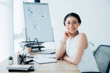 ofiste işyerinde otururken kameraya gülümseyen gözlük neşeli latin iş kadını