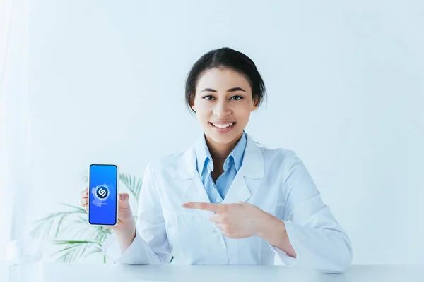 乌克兰 2019年4月26日 微笑的拉丁医生用手指指着智能手机与沙扎姆应用程序在屏幕上 — 图库照片