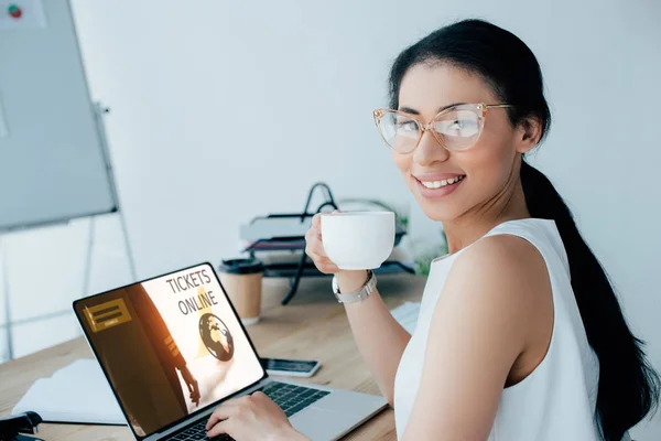 漂亮的拉丁女商人拿着咖啡杯 同时使用笔记本电脑与门票在线网站在屏幕上 — 图库照片