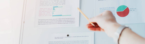 panoramic shot of businesswoman pointing at flipchart with graphs and charts