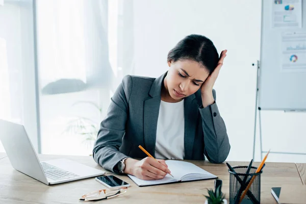 Exhausted Latin Businesswoman Writing Notebook While Sitting Desk Holding Hand — Stock Photo, Image