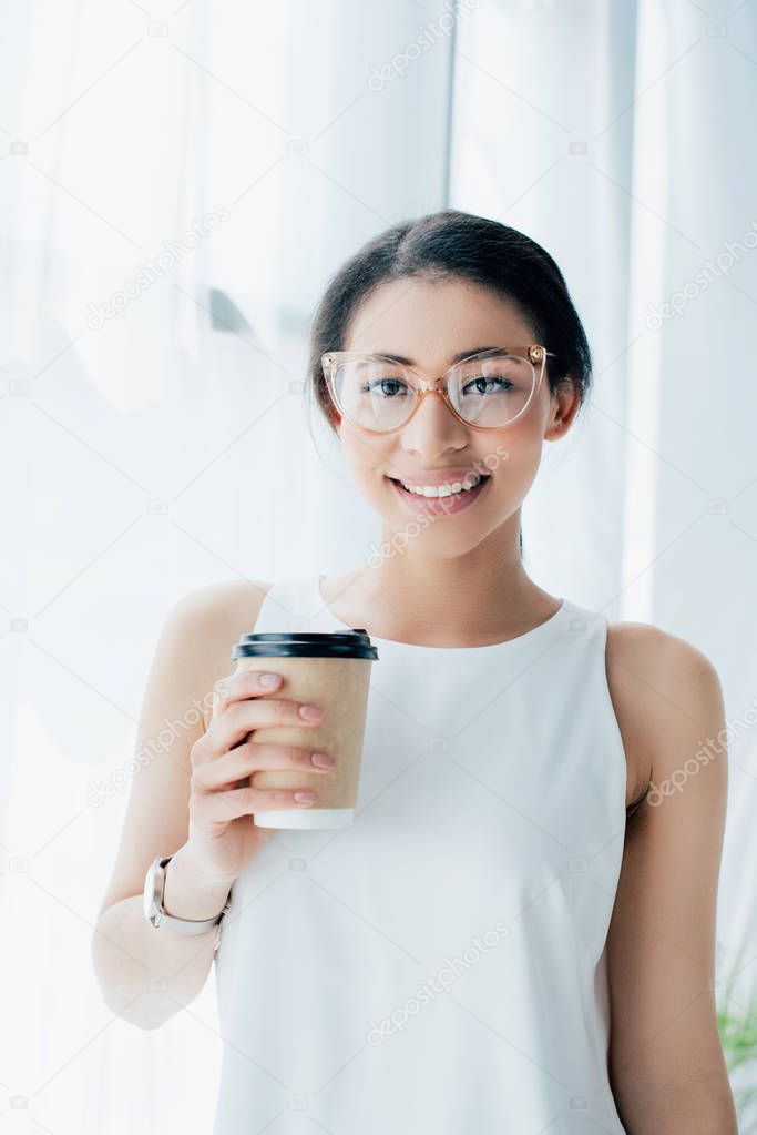 cheerful latin businesswoman smiling at camera while holding coffee to go