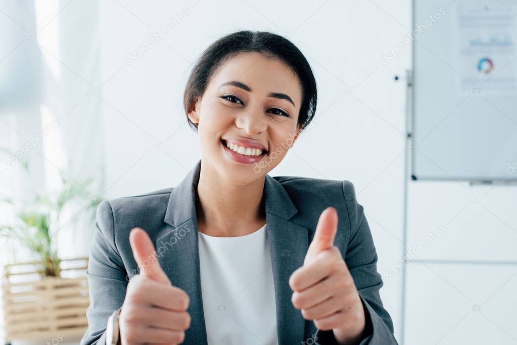 cheerful latin businesswoman showing thumbs up while smiling at camera
