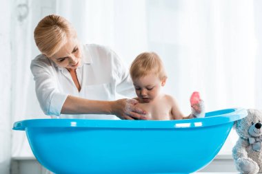 evde sarışın anne yakınında banyo alarak sevimli yürümeye başlayan çocuk 