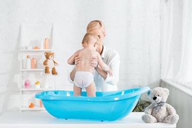 sarışın anne banyoda kollarında yürümeye başlayan çocuk tutarak 