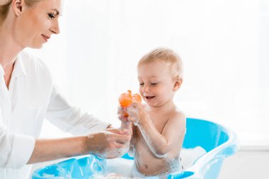 mutlu anne banyoda kauçuk ördek tutan neşeli yürümeye başlayan oğlu yıkama 