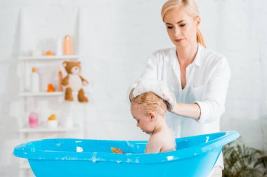 banyoda sevimli yürümeye başlayan çocuğun sarışın anne yıkama kafası seçici odak 