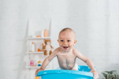 banyo ve evde mavi plastik bebek küvetinde gülümseyen yürümeye başlayan çocuk