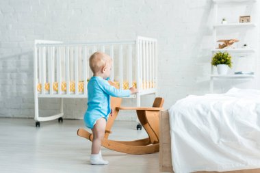 sevimli yürümeye başlayan çocuk modern yatak odasında ahşap sallanan at yakınında duran 