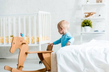 sevimli yürümeye başlayan çocuk modern yatak odasında ahşap sallanan at yanında duran 