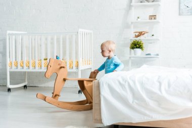 modern yatak odasında ahşap sallanan at yakınında sevimli yürümeye başlayan çocuk 