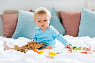 yatakta renkli oyuncak blokları yakınında ahşap çift kanatlı ile oynayan yeni yürümeye başlayan çocuk 