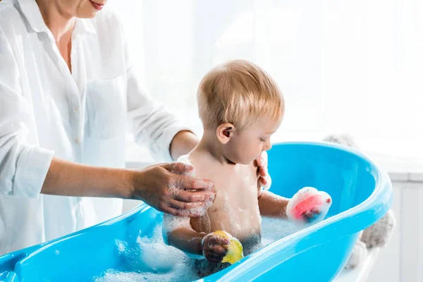 バスルームでかわいい幼児の息子を洗う母親のトリミングビュー — ストック写真
