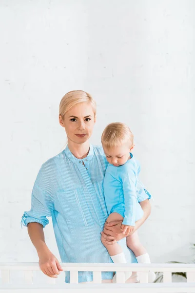 Attractive Mother Holding Arms Toddler Son Standing Baby Crib Home — Stock Photo, Image