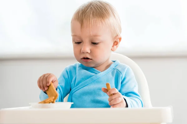 自宅でおいしいクッキーの近くに給餌椅子に座ってかわいい幼児の子供 — ストック写真