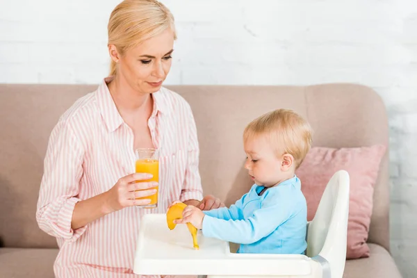 Rubia Madre Celebración Vidrio Con Zumo Naranja Cerca Lindo Niño —  Fotos de Stock