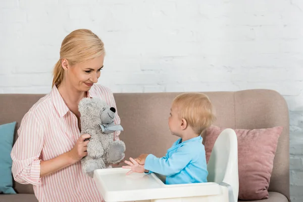 Alegre Madre Sosteniendo Osito Peluche Cerca Lindo Niño Hijo Alimentación — Foto de Stock