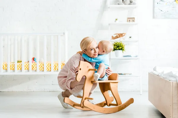 Lindo Niño Hijo Abrazando Feliz Rubia Madre Cerca Balanceo Caballo — Foto de Stock