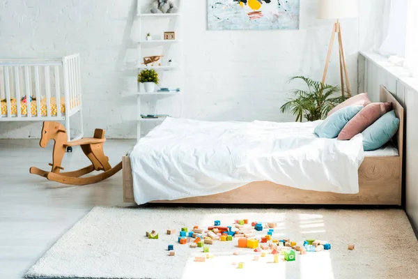 カーペットの上に白い寝具とおもちゃのブロックとベッドの近くに木製のロッキングホース — ストック写真