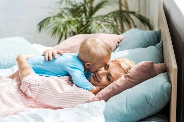 Cheerful Blonde Mother Hugging Cute Toddler Son While Lying Bed — Stock Photo, Image