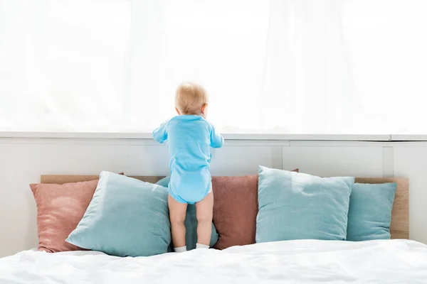 ベッドの上に立って寝室の窓を見ている幼児の子供の背面図 — ストック写真