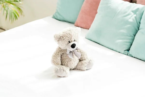 grey teddy bear near pink and blue pillows on white bedding in bedroom