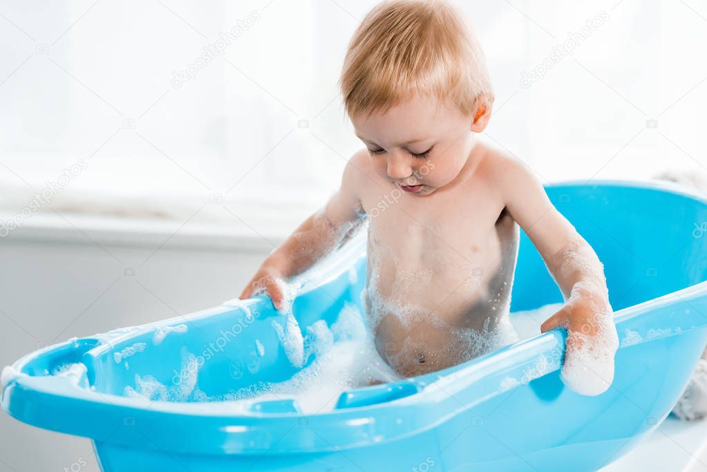 adorable toddler kid taking bath and looking at bath foam 