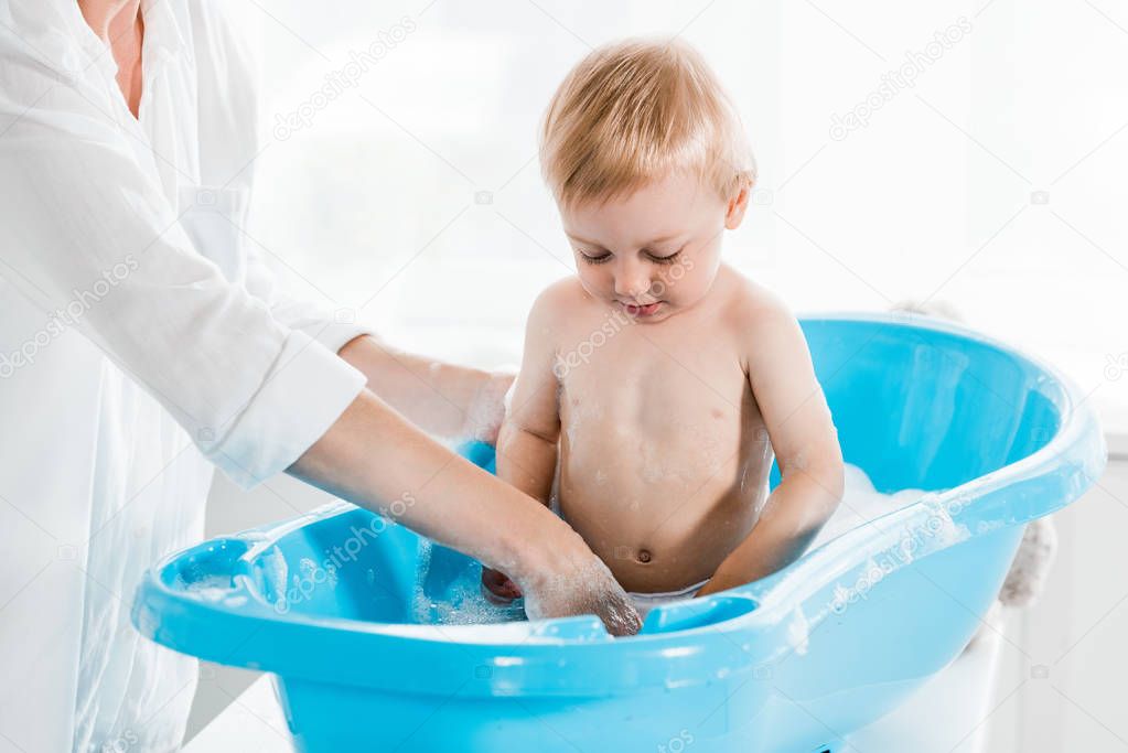 cropped view of mother standing near cute toddler son in bathroom 