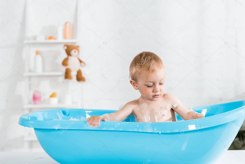 cute toddler kid taking bath and looking at bath foam 