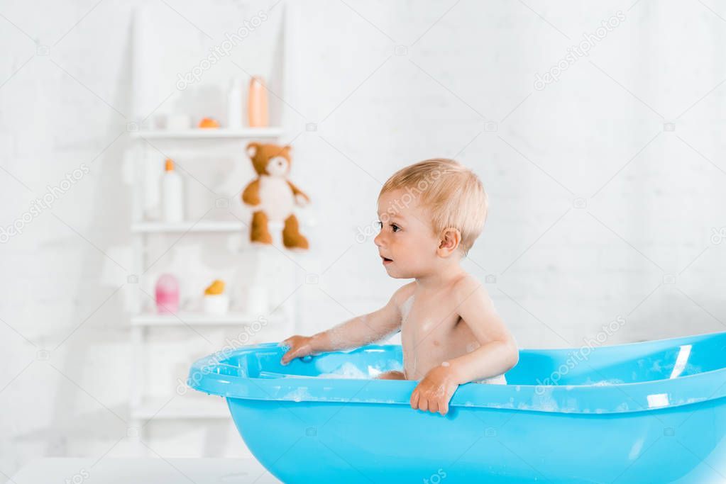 adorable toddler kid taking bath in blue baby bathtub 