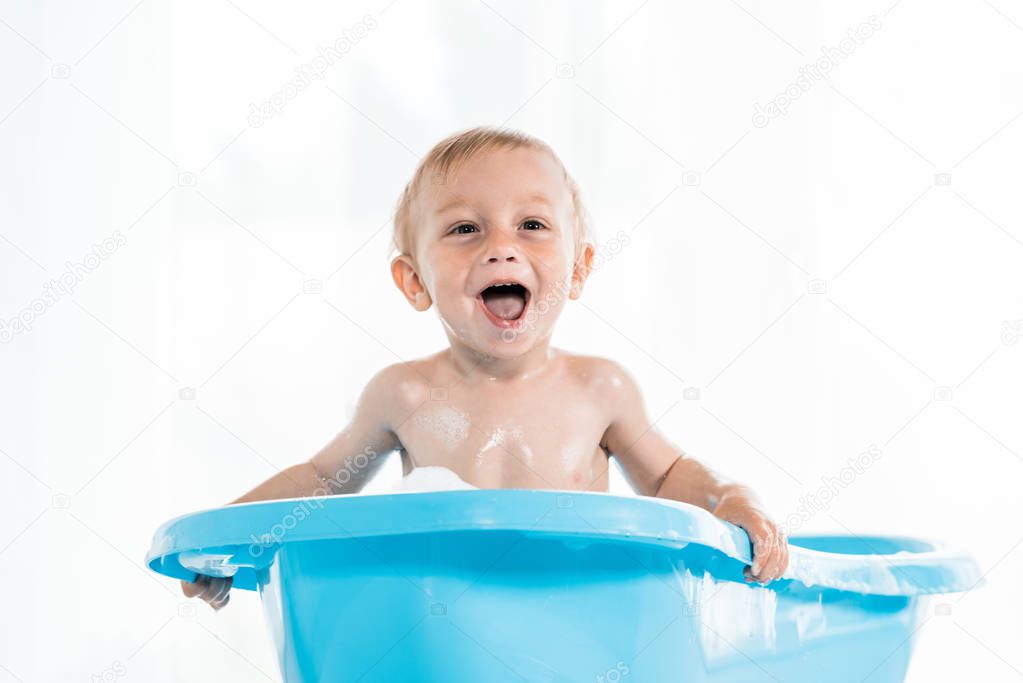 adorable toddler kid smiling while taking bath in blue baby bathtub 