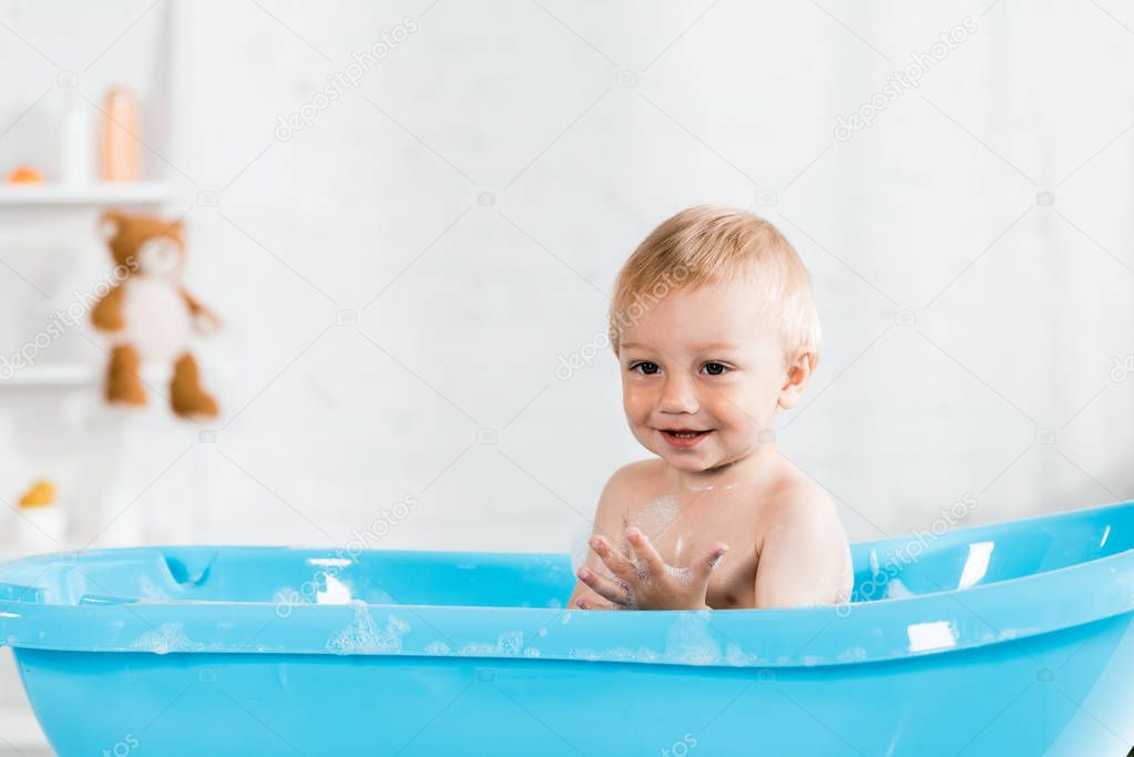 cute toddler kid smiling while taking bath in blue baby bathtub 
