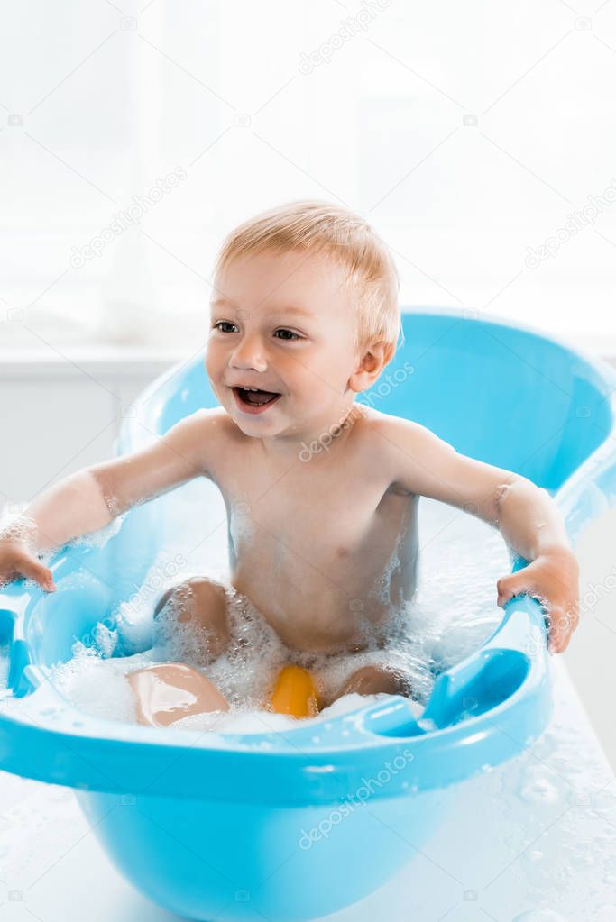 happy toddler kid smiling while taking bath in blue baby bathtub 