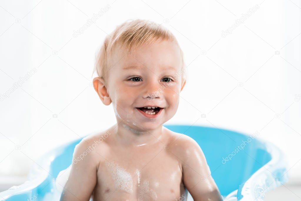 happy toddler kid smiling while taking bath in plastic baby bathtub 
