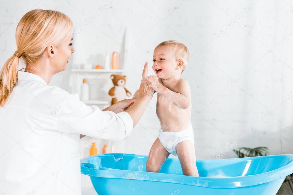 blonde mother pointing with finger at cute toddler son in bathroom 