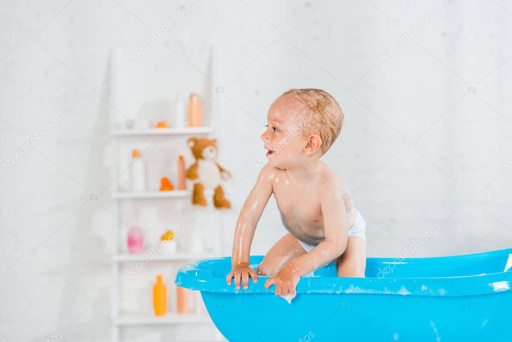 naked and cute toddler kid smiling in plastic baby bathtub 