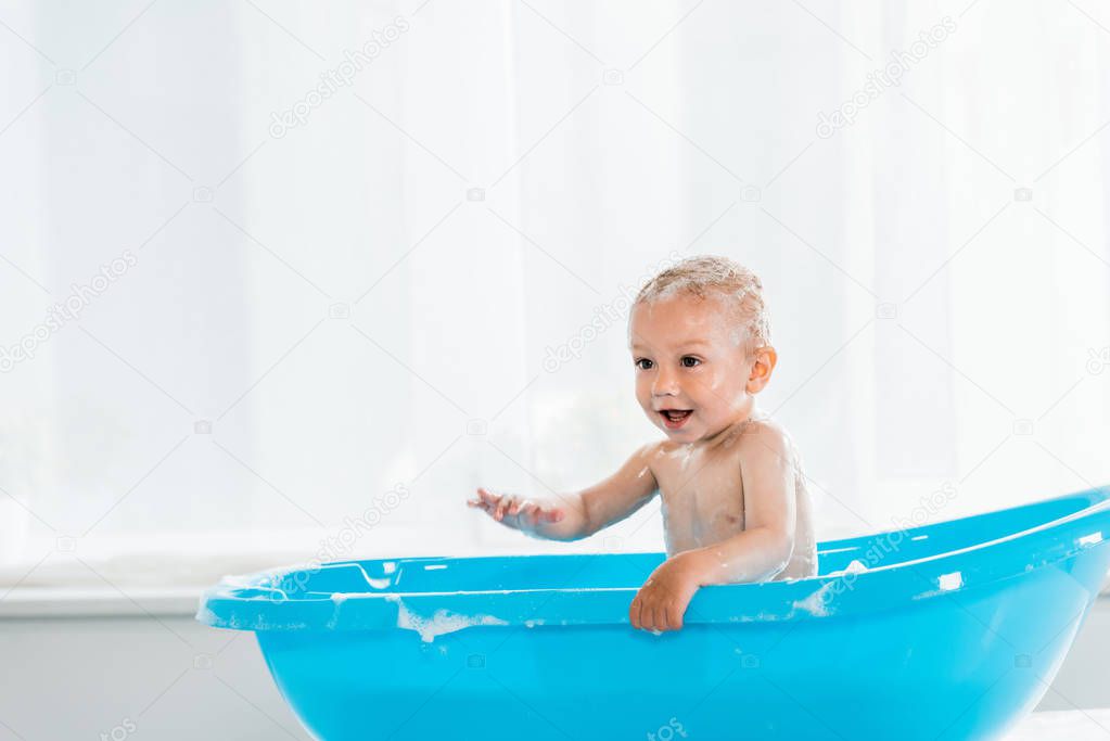adorable toddler child taking bath and smiling in blue plastic baby bathtub 