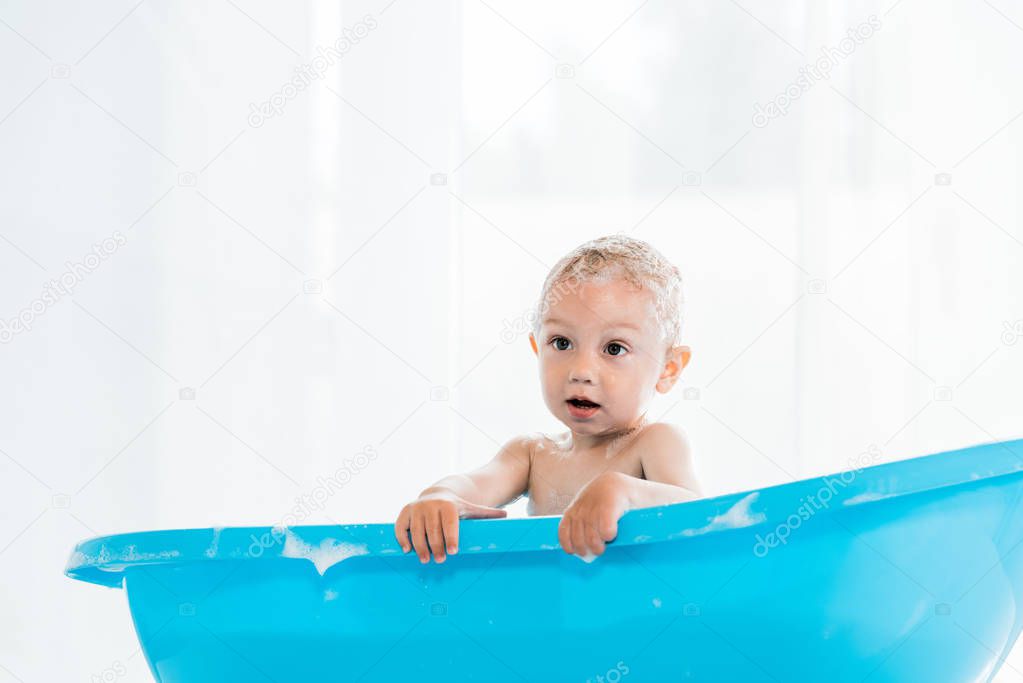 adorable toddler kid taking bath in blue plastic baby bathtub 