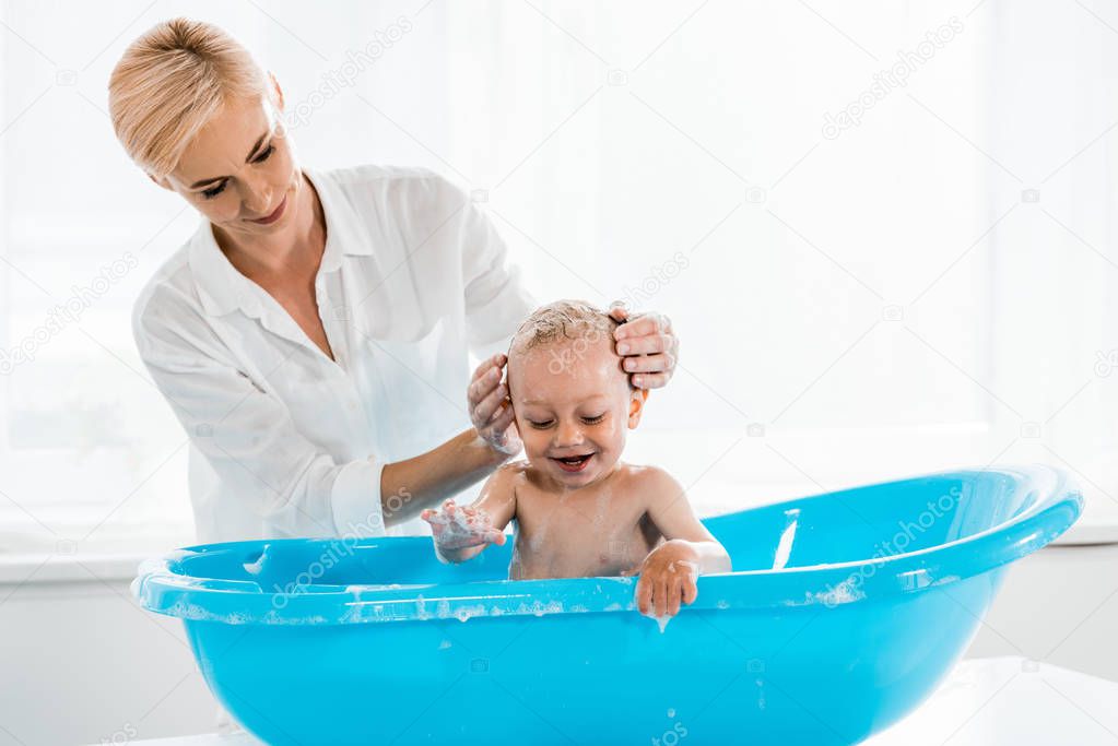 attractive blonde mother washing head of toddler son in bathroom 