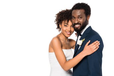 cheerful african american bridegroom and bride hugging and looking at camera isolated on white  clipart