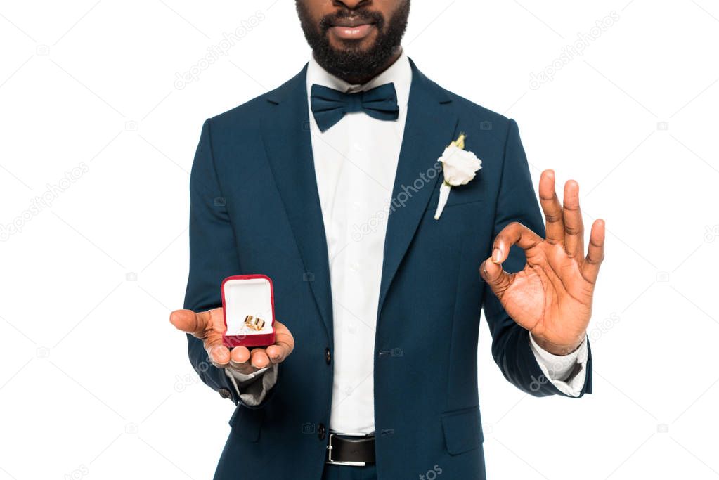 cropped view of african american man holding box with wedding ring and showing ok sign isolated on white 