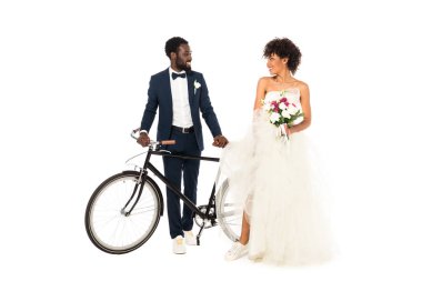 happy african american bridegroom near bride with flowers holding bicycle isolated on white  clipart