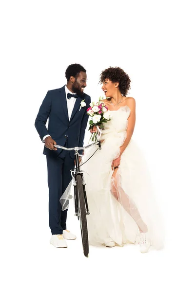 白に隔離された自転車を持つ花を持つ陽気な花嫁の近くに幸せなアフリカ系アメリカ人の花婿 — ストック写真
