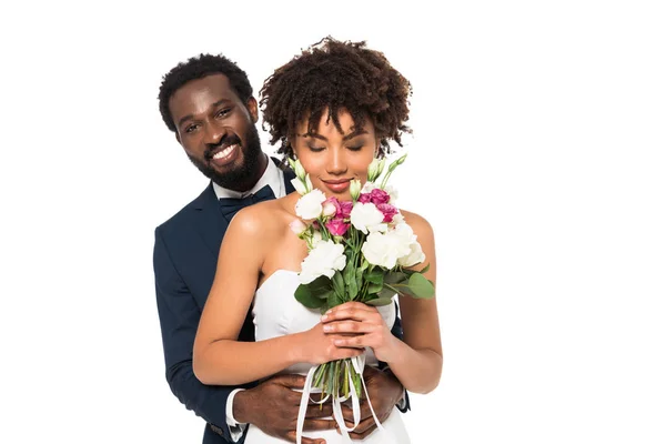 Smiling African American Bridegroom Hugging Attractive Bride Smelling Flowers Isolated Stock Photo